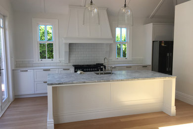 Inspiration for a mid-sized victorian galley medium tone wood floor eat-in kitchen remodel in Auckland with an undermount sink, recessed-panel cabinets, white cabinets, marble countertops, white backsplash, ceramic backsplash, black appliances, an island and gray countertops