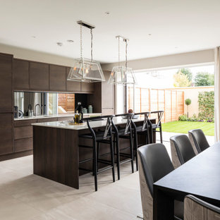 Design ideas for a large contemporary galley kitchen/diner in London with a submerged sink, flat-panel cabinets, medium wood cabinets, white splashback, mirror splashback, black appliances, porcelain flooring, an island, beige floors and brown worktops.