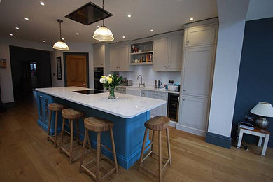 Inspiration for a classic single-wall kitchen/diner in Other with a belfast sink, shaker cabinets, grey cabinets, quartz worktops, white splashback, integrated appliances and an island.