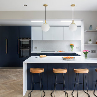Medium sized contemporary u-shaped kitchen in London with marble worktops, white splashback, ceramic splashback, black appliances, light hardwood flooring, a breakfast bar, white worktops, flat-panel cabinets, blue cabinets and beige floors.