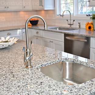 Modelo de cocina comedor en L, contemporánea, con fregadero bajoencimera, armarios estilo shaker, puertas de armario blancas, encimera de granito, salpicadero blanco, salpicadero de azulejos tipo metro, electrodomésticos de acero inoxidable, suelo de baldosas de cerámica y una isla