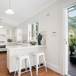 Mid-sized transitional u-shaped kitchen in Sydney with a double-bowl sink, beaded inset cabinets, white cabinets, laminate benchtops, subway tile splashback, white appliances, medium hardwood floors, a peninsula, brown floor, white benchtop and white splashback.