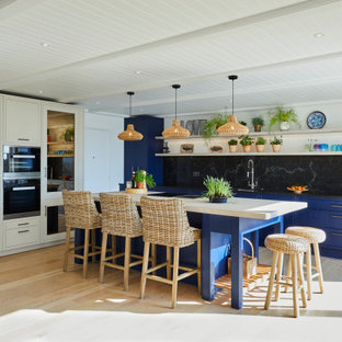 Design ideas for a medium sized nautical single-wall open plan kitchen in Kent with a submerged sink, beaded cabinets, blue cabinets, quartz worktops, black splashback, stainless steel appliances, laminate floors, an island, beige floors and black worktops.
