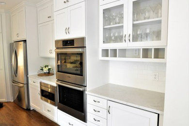 This is an example of a medium sized classic u-shaped kitchen/diner in Atlanta with a submerged sink, shaker cabinets, white cabinets, engineered stone countertops, white splashback, porcelain splashback, stainless steel appliances, dark hardwood flooring, an island, brown floors and white worktops.