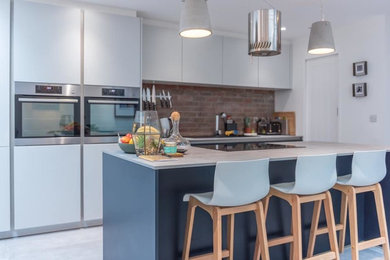 Medium sized modern single-wall kitchen/diner in Cardiff with an integrated sink, flat-panel cabinets, blue cabinets, concrete worktops, red splashback, brick splashback, stainless steel appliances, concrete flooring, an island, grey floors and grey worktops.