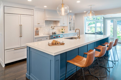 Beach style brown floor and dark wood floor kitchen photo in Boston with white cabinets, white backsplash, marble backsplash, paneled appliances, an island, white countertops, an undermount sink and shaker cabinets