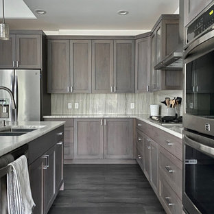 Modern l-shaped open plan kitchen in Seattle with a farmhouse sink, raised-panel cabinets, brown cabinets, marble benchtops, white splashback, granite splashback, stainless steel appliances, vinyl floors, with island, brown floor and white benchtop.