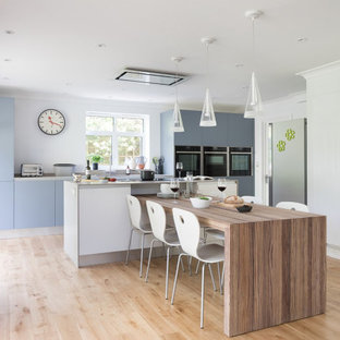 Inspiration for a large contemporary galley kitchen/diner in London with flat-panel cabinets, blue cabinets, laminate countertops, black appliances, laminate floors, an island, grey worktops and beige floors.