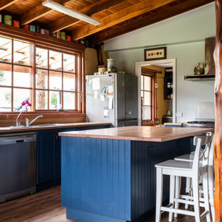 This is an example of a country galley kitchen in Hobart with a drop-in sink, blue cabinets, wood benchtops, stainless steel appliances, dark hardwood floors, with island, brown floor and brown benchtop.