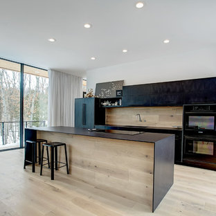 Inspiration for a mid-sized modern galley open plan kitchen in Grand Rapids with an integrated sink, flat-panel cabinets, black cabinets, quartz benchtops, timber splashback, black appliances, light hardwood floors, with island and beige floor.