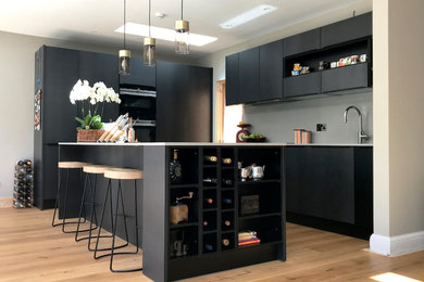 Inspiration for a medium sized urban open plan kitchen in London with a single-bowl sink, flat-panel cabinets, blue cabinets, granite worktops, white splashback, black appliances, an island, brown floors and white worktops.