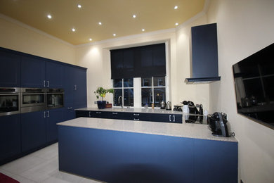 Imagen de cocina comedor contemporánea de tamaño medio con fregadero integrado, puertas de armario azules, electrodomésticos de acero inoxidable, suelo de baldosas de porcelana y una isla