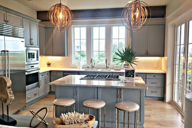 Klassische Küche in L-Form mit Schrankfronten im Shaker-Stil, grauen Schränken, Küchengeräten aus Edelstahl und Kücheninsel in Sonstige