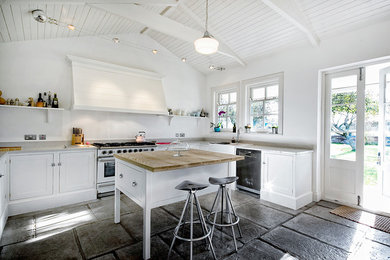 This is an example of a farmhouse u-shaped kitchen in Other with a belfast sink, recessed-panel cabinets, white cabinets, stainless steel appliances and an island.