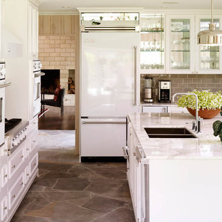 Inspiration for a traditional kitchen in Dallas with a double-bowl sink, glass-front cabinets, white cabinets, grey splashback, subway tile splashback, white appliances and slate floors.