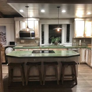 Mid-sized country l-shaped eat-in kitchen in Hawaii with an undermount sink, recessed-panel cabinets, distressed cabinets, concrete benchtops, multi-coloured splashback, glass tile splashback, stainless steel appliances, laminate floors, with island and brown floor.