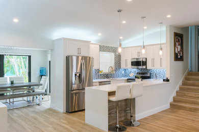 Inspiration for a transitional u-shaped kitchen remodel in Miami with an undermount sink, shaker cabinets, white cabinets, quartz countertops, gray backsplash, subway tile backsplash, stainless steel appliances, an island and white countertops