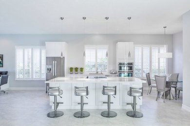 Mid-sized trendy single-wall porcelain tile and gray floor eat-in kitchen photo in Miami with flat-panel cabinets, white cabinets, quartzite countertops, stainless steel appliances, an island, a single-bowl sink, white backsplash and stone slab backsplash