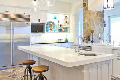 Large elegant u-shaped limestone floor and brown floor eat-in kitchen photo in Austin with a farmhouse sink, raised-panel cabinets, white cabinets, glass countertops, white backsplash, marble backsplash, stainless steel appliances, an island and yellow countertops