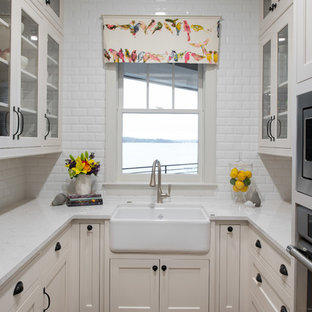 Small beach style u-shaped kitchen in Minneapolis with a farmhouse sink, glass-front cabinets, beige cabinets, white splashback, subway tile splashback, stainless steel appliances, dark hardwood floors, no island and white benchtop.