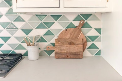 Foto di una cucina con ante con bugna sagomata, ante bianche, top in quarzo composito, paraspruzzi verde e top bianco