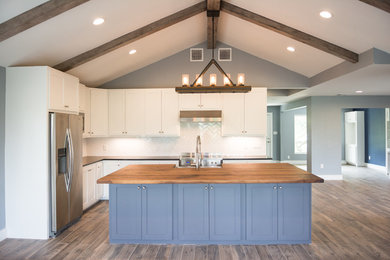 Example of a mid-sized trendy l-shaped vinyl floor and brown floor open concept kitchen design in Houston with a farmhouse sink, shaker cabinets, white cabinets, solid surface countertops, stainless steel appliances and an island