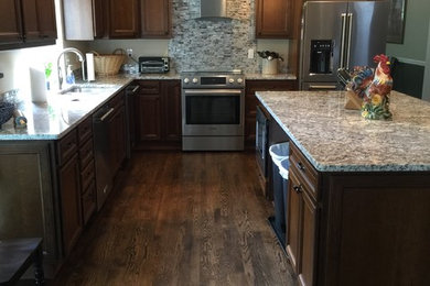 Inspiration for a large timeless l-shaped dark wood floor and brown floor eat-in kitchen remodel in Boise with a drop-in sink, recessed-panel cabinets, dark wood cabinets, granite countertops, multicolored backsplash, glass sheet backsplash, stainless steel appliances, an island and multicolored countertops