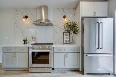 Klassisk inredning av ett mellanstort vit vitt kök, med en undermonterad diskho, skåp i shakerstil, grå skåp, bänkskiva i kvartsit, vitt stänkskydd, stänkskydd i stenkakel, rostfria vitvaror, laminatgolv och en halv köksö