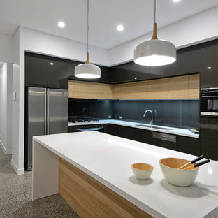 Inspiration for a contemporary l-shaped kitchen in Sunshine Coast with a double-bowl sink, flat-panel cabinets, black cabinets, black splashback, glass sheet splashback, black appliances, concrete floors, with island, grey floor and white benchtop.