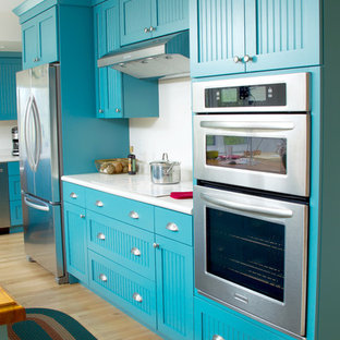 Design ideas for a mid-sized eclectic l-shaped eat-in kitchen in Milwaukee with turquoise cabinets, white splashback, stainless steel appliances, light hardwood floors, with island, a single-bowl sink, flat-panel cabinets, yellow floor and white benchtop.