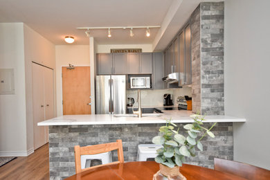 Example of a mid-sized urban u-shaped laminate floor eat-in kitchen design in Other with an undermount sink, shaker cabinets, gray cabinets, quartz countertops, white backsplash, porcelain backsplash, stainless steel appliances and white countertops