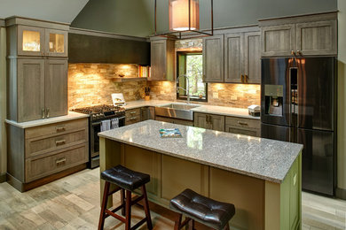 Trendy galley medium tone wood floor and gray floor eat-in kitchen photo in Other with a farmhouse sink, flat-panel cabinets, gray cabinets, quartzite countertops, beige backsplash, travertine backsplash, black appliances, an island and gray countertops