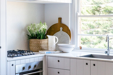 На фото: маленькая угловая кухня в морском стиле с белыми фасадами, белым фартуком, фартуком из плитки мозаики, техникой из нержавеющей стали и окном для на участке и в саду