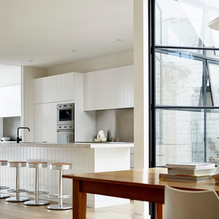 Design ideas for a large scandinavian single-wall open plan kitchen in Sydney with louvered cabinets, white cabinets, limestone benchtops, grey splashback, stainless steel appliances, light hardwood floors, with island, brown floor and white benchtop.