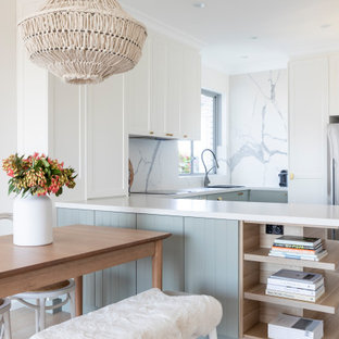 Photo of a small beach style u-shaped eat-in kitchen in Sydney with an undermount sink, shaker cabinets, white cabinets, quartz benchtops, white splashback, marble splashback, stainless steel appliances, light hardwood floors, white benchtop, a peninsula and beige floor.