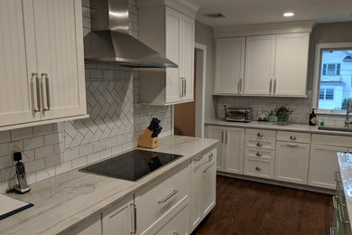 Transitional dark wood floor and brown floor kitchen photo in New York with a single-bowl sink, shaker cabinets, white cabinets, quartzite countertops, white backsplash, ceramic backsplash, stainless steel appliances, an island and white countertops