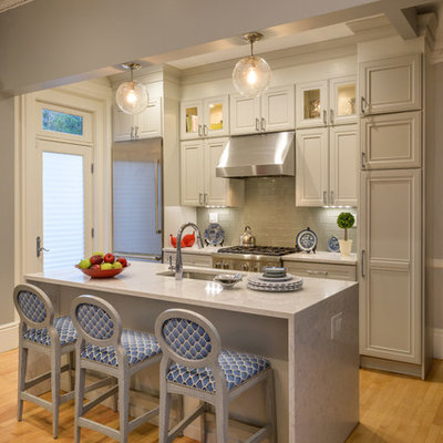 Example of a classic galley medium tone wood floor and brown floor kitchen design in Boston with an undermount sink, recessed-panel cabinets, gray cabinets, gray backsplash, subway tile backsplash, stainless steel appliances, an island and white countertops