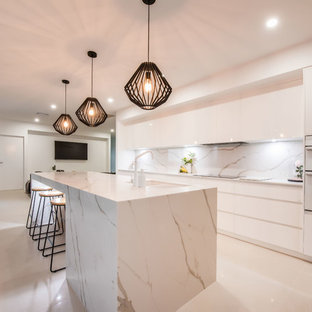 This is an example of a large contemporary galley open plan kitchen in Other with flat-panel cabinets, white splashback, marble splashback, white appliances, white benchtop, with island, an undermount sink, light wood cabinets, marble benchtops, ceramic floors and white floor.