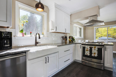 Eat-in kitchen - mid-sized transitional l-shaped vinyl floor and brown floor eat-in kitchen idea in Denver with a farmhouse sink, shaker cabinets, granite countertops, white backsplash, ceramic backsplash, stainless steel appliances, a peninsula and gray countertops