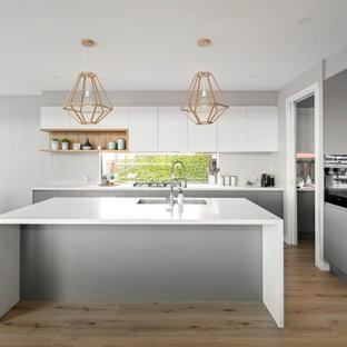Large contemporary l-shaped kitchen in Melbourne with an undermount sink, flat-panel cabinets, grey cabinets, white splashback, porcelain splashback, panelled appliances, with island, beige floor and white benchtop.