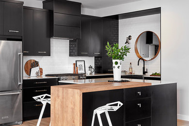 Inspiration for a contemporary l-shaped medium tone wood floor and brown floor kitchen remodel in Edmonton with a farmhouse sink, flat-panel cabinets, black cabinets, white backsplash, stainless steel appliances, an island and white countertops