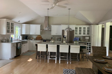 Inspiration for a mid-sized transitional l-shaped light wood floor eat-in kitchen remodel in Boston with a farmhouse sink, shaker cabinets, white cabinets, quartz countertops, stainless steel appliances, an island and beige countertops