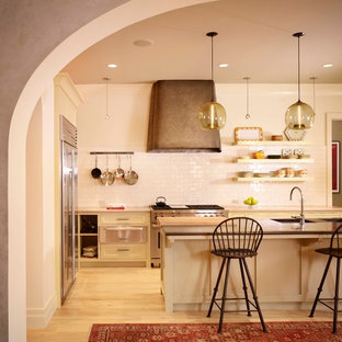 Inspiration for a mediterranean kitchen in Austin with shaker cabinets, beige cabinets, white splashback, subway tile splashback, stainless steel appliances, light hardwood floors and with island.
