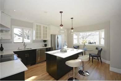 Example of a mid-sized trendy l-shaped light wood floor enclosed kitchen design in Calgary with an undermount sink, raised-panel cabinets, white cabinets, white backsplash, stainless steel appliances and an island