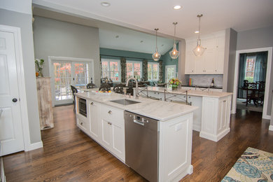 Large trendy medium tone wood floor open concept kitchen photo in Boston with an undermount sink, shaker cabinets, white cabinets, marble countertops, white backsplash, subway tile backsplash, stainless steel appliances and two islands