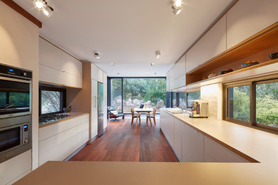 Moderne Wohnküche in L-Form mit weißen Schränken, Laminat-Arbeitsplatte, Rückwand-Fenster, Küchengeräten aus Edelstahl, Doppelwaschbecken, dunklem Holzboden und rotem Boden in Perth