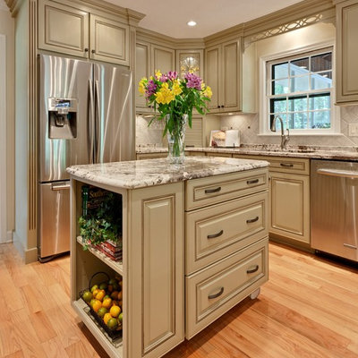 Mid-sized elegant l-shaped light wood floor and brown floor eat-in kitchen photo in Atlanta with raised-panel cabinets, stainless steel appliances, an undermount sink, green cabinets, granite countertops, beige backsplash, stone tile backsplash, an island and beige countertops