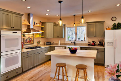 Example of a mid-sized arts and crafts l-shaped medium tone wood floor and brown floor kitchen design in Other with a farmhouse sink, shaker cabinets, green cabinets, white appliances, an island and beige countertops