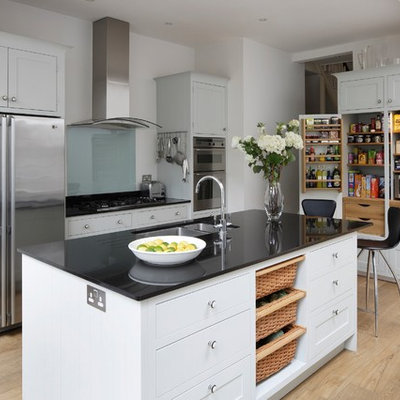 Mid-sized transitional single-wall medium tone wood floor open concept kitchen photo in London with a drop-in sink, shaker cabinets, white cabinets, granite countertops, glass sheet backsplash, stainless steel appliances, an island and black countertops