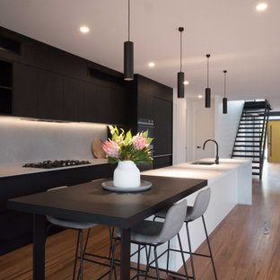 Design ideas for a large contemporary kitchen in Melbourne with an undermount sink, black cabinets, grey splashback, black appliances, medium hardwood floors, with island, brown floor and grey benchtop.